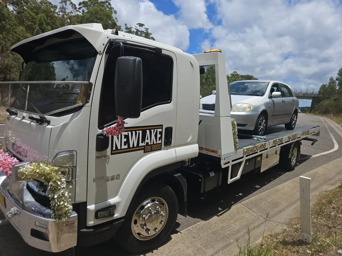 NewLake tilt tray carrying a silver sedan beside a kerb