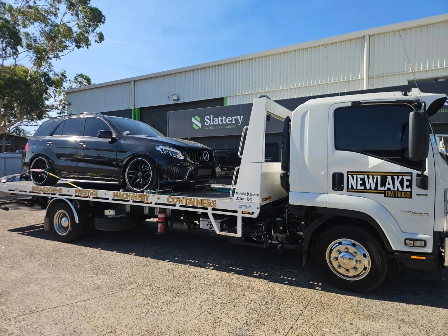 NewLake tilt tray carrying a black SUV outside a commercial building